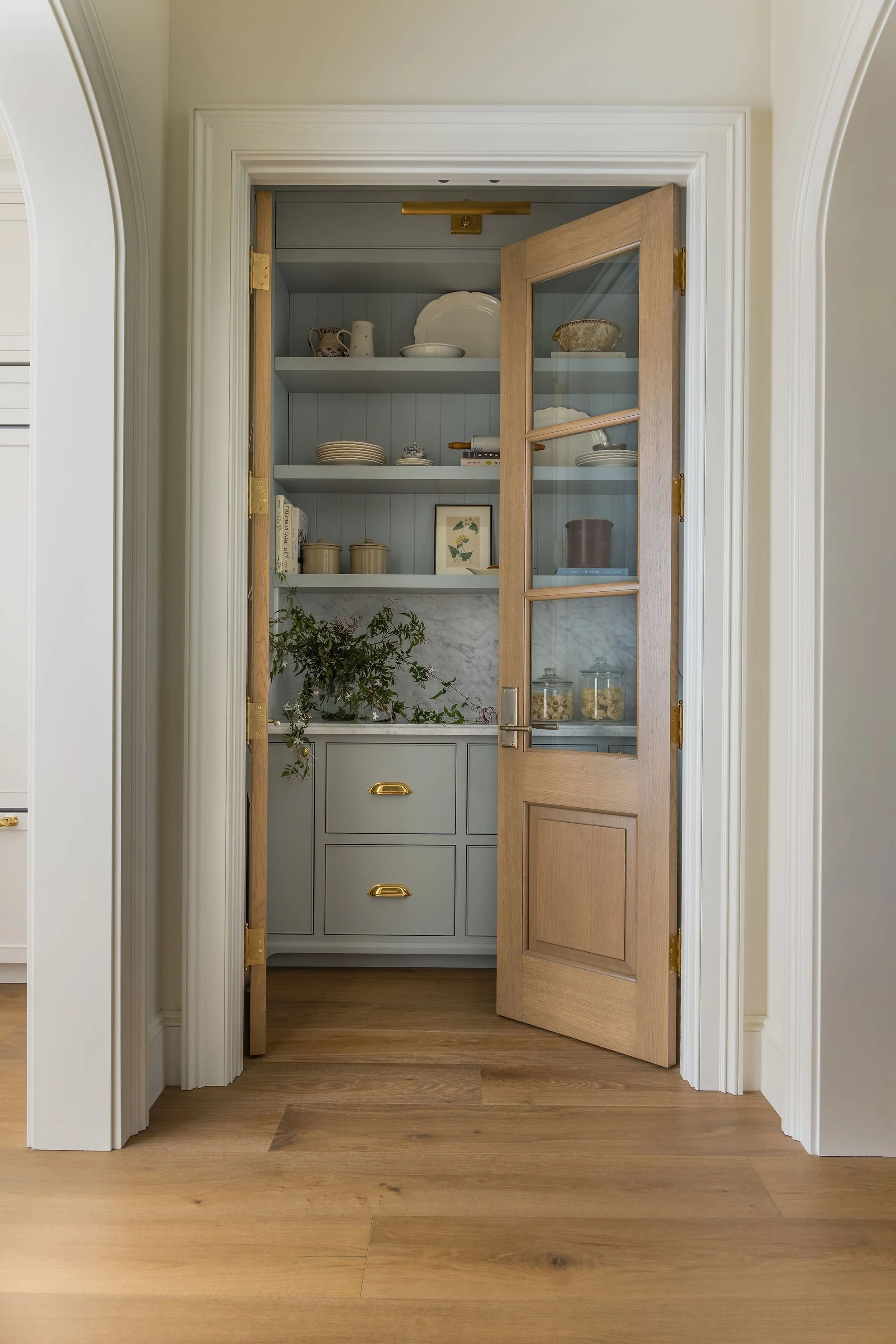 Open kitchen cabinet with two doors, blue interior, and dishes inside. The cabinet is located within a doorway with white trim and a marble countertop below. The floor is wood.
