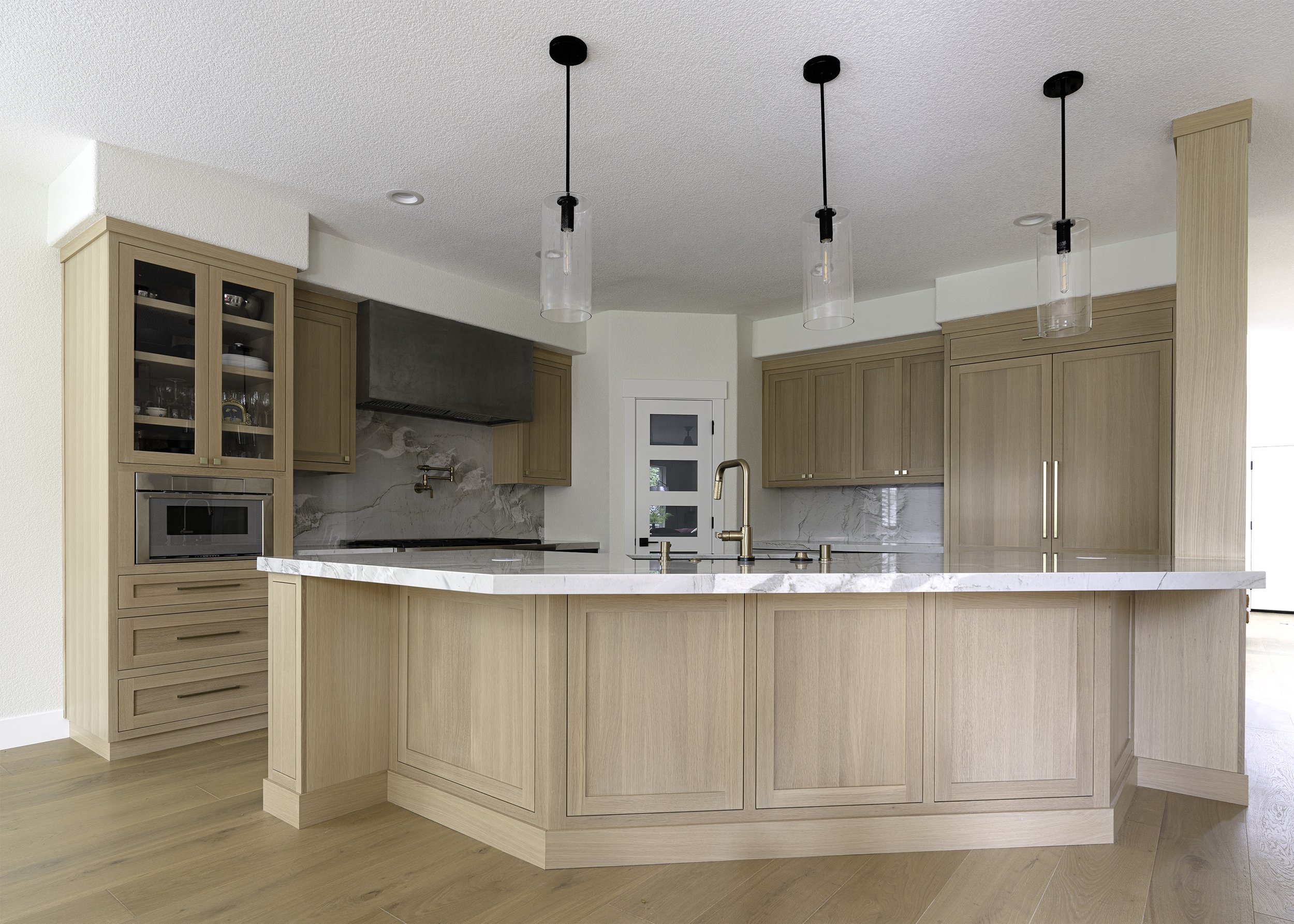 Modern kitchen with a large wooden island, light wood cabinets, marble backsplash, and pendant lights.