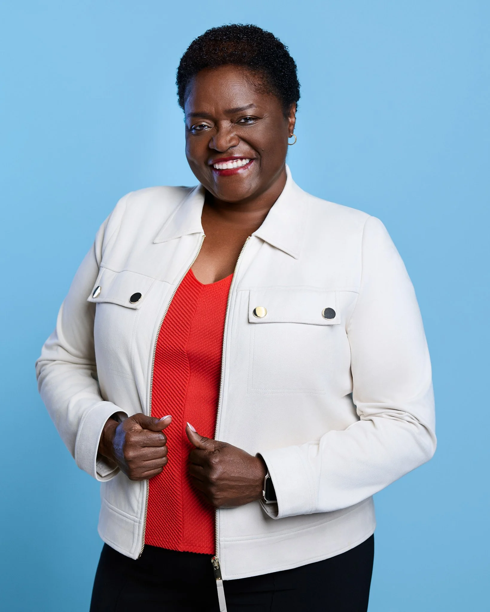 Vivica smiling and holding the collar of her white jacket against a blue background.