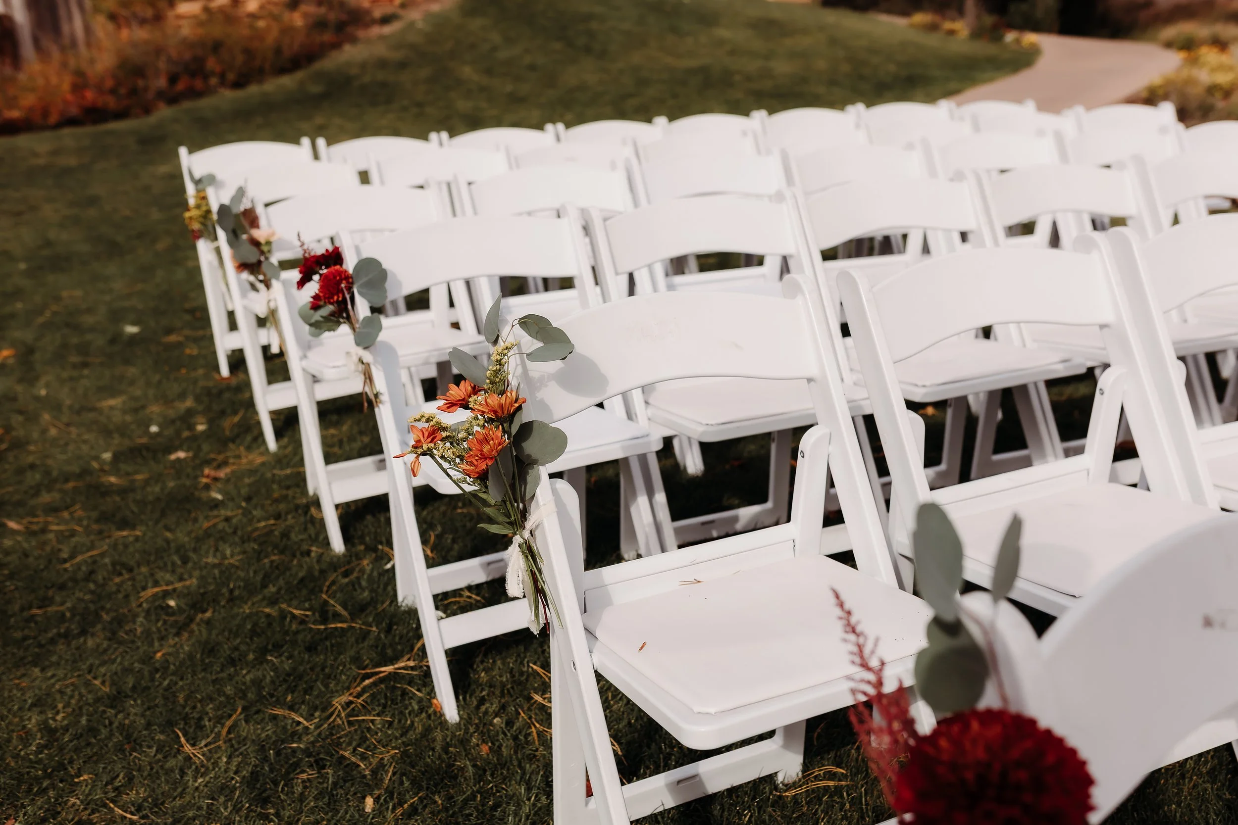 White folding chairs decorated with floral arrangements on a grassy outdoor setting.