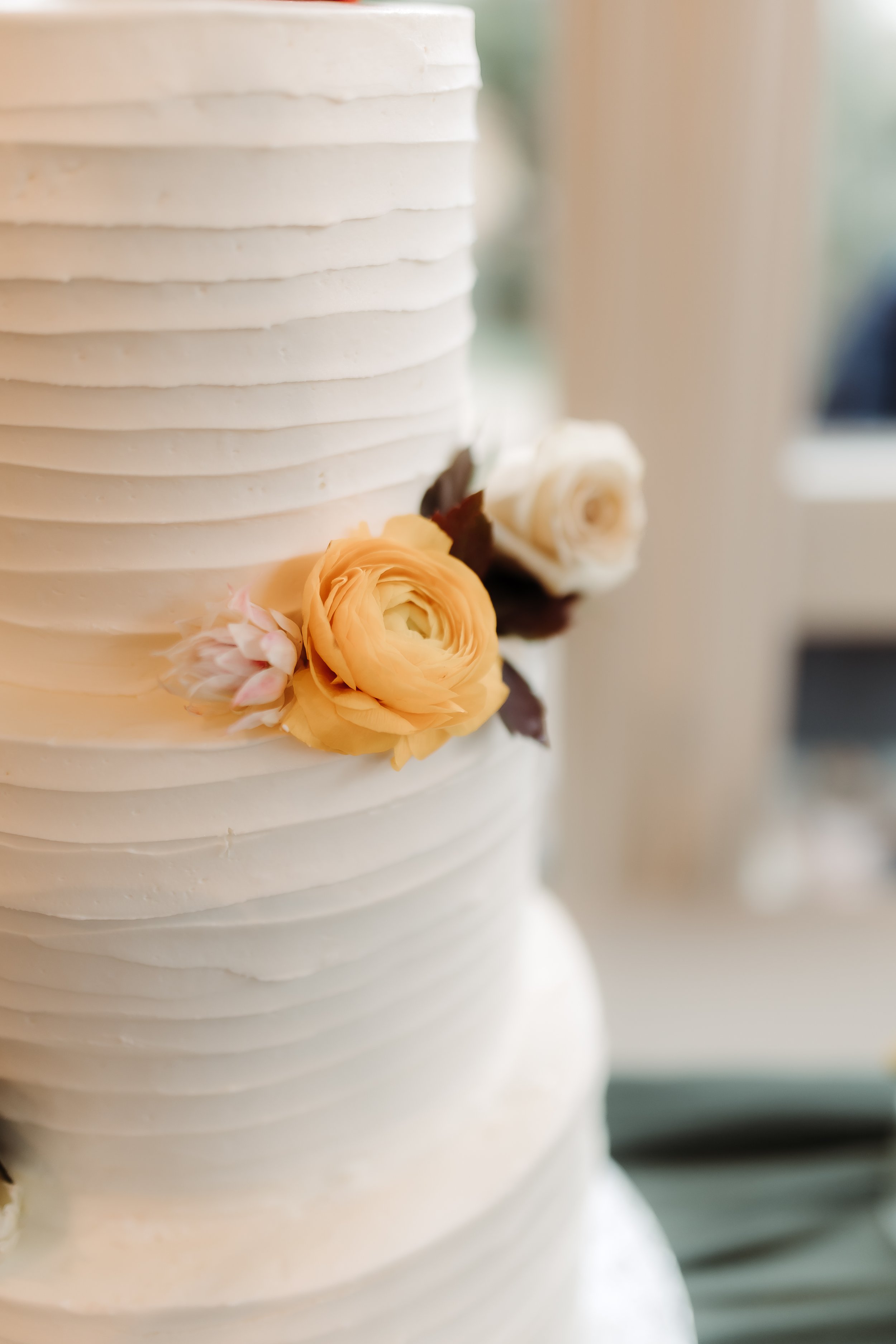 Close-up of a white wedding cake with horizontal ridges, decorated with peach, white, and pink flowers.