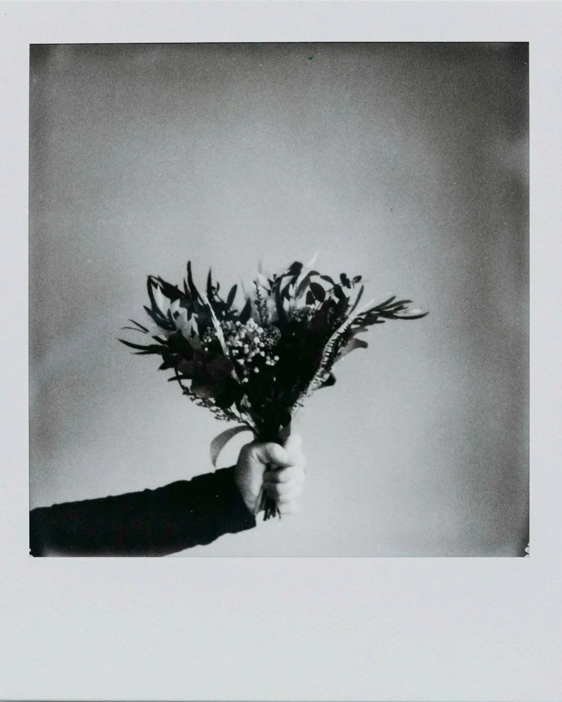 A person's hand holding a bouquet of flowers in front of a plain wall.