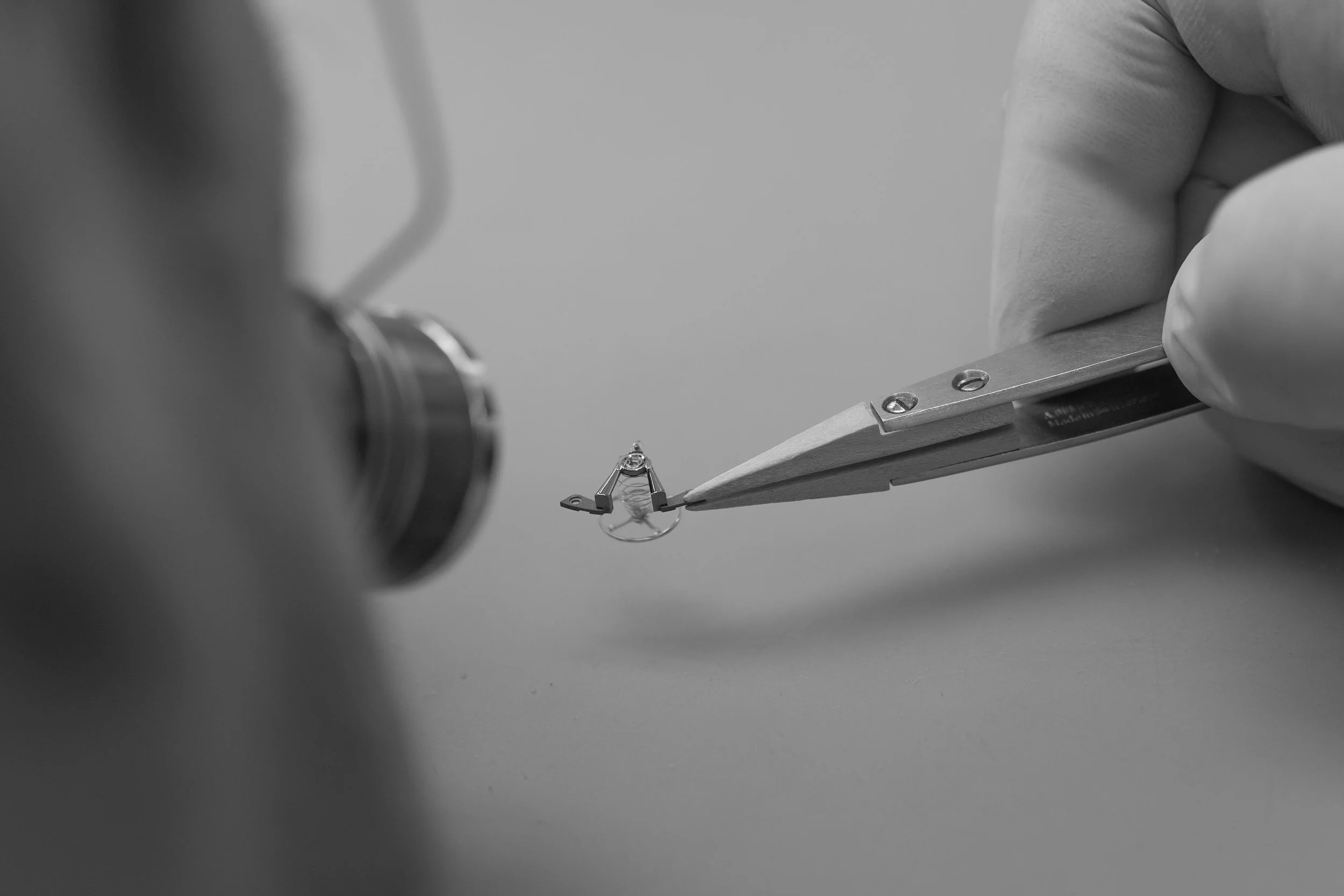 A person wearing gloves is using tweezers to inspect a small balance bridge.