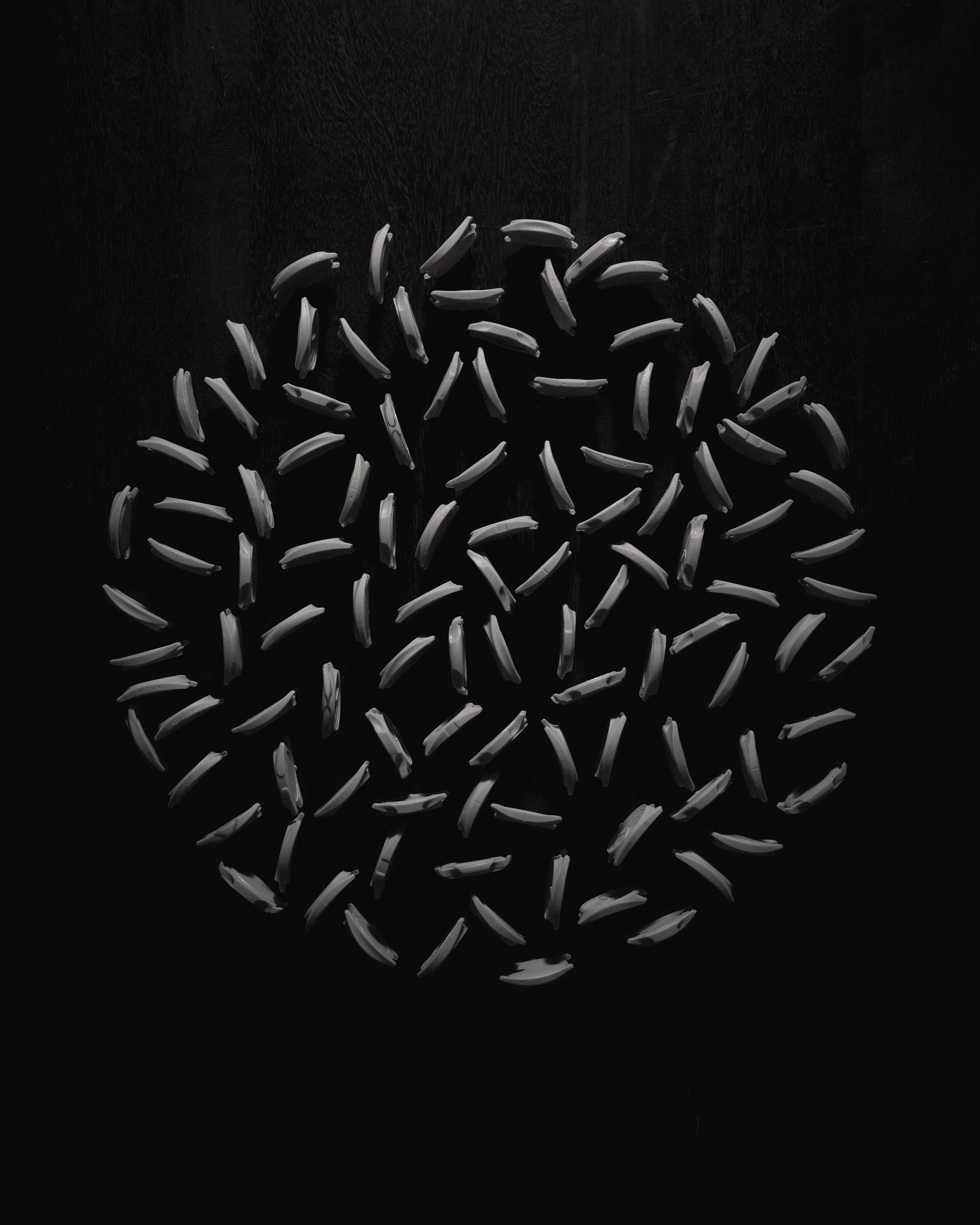 Numerous gray 3-D printed case profiles scattered on a black surface with a dark background.
