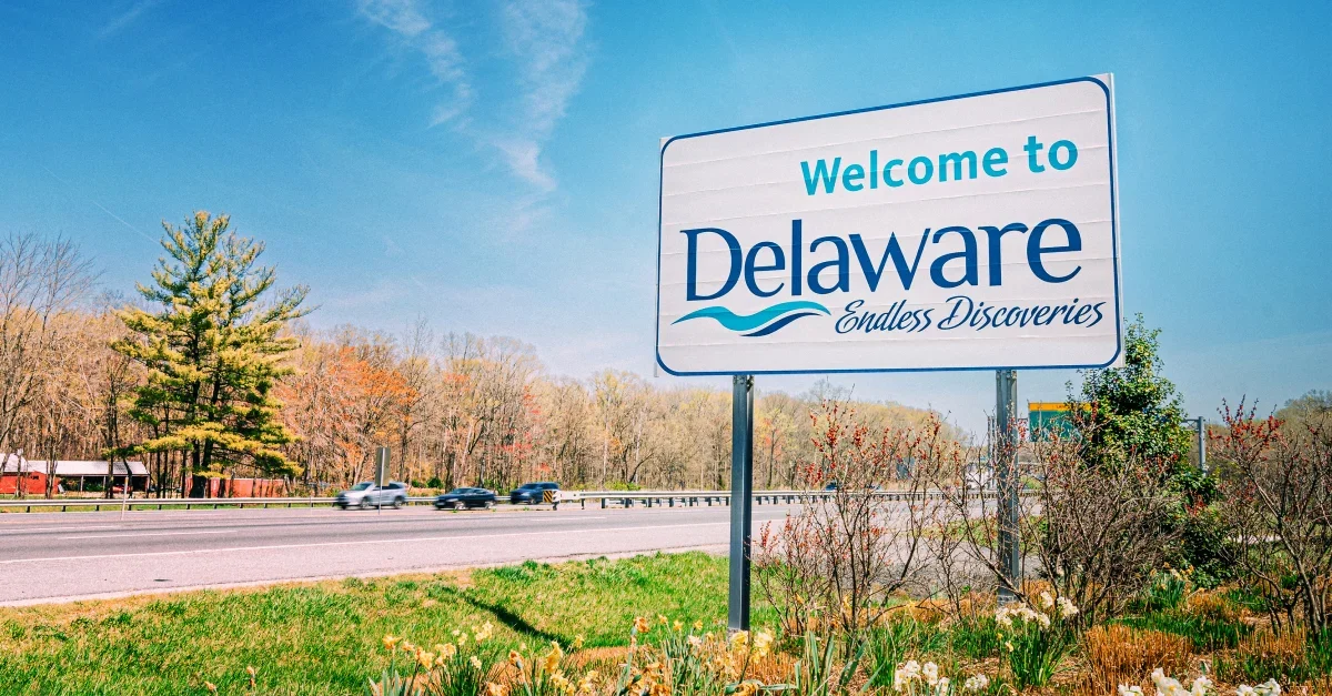 Welcome to Delaware sign on roadside with trees and cars in the background on a sunny day.