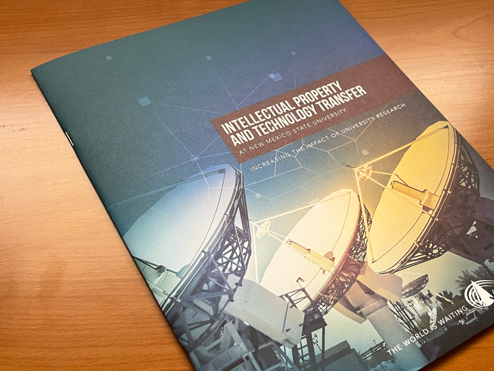 A brochure titled 'Intellectual Property and Technology Transfer at New Mexico State University' with an image of large satellite dishes, on a wooden surface.