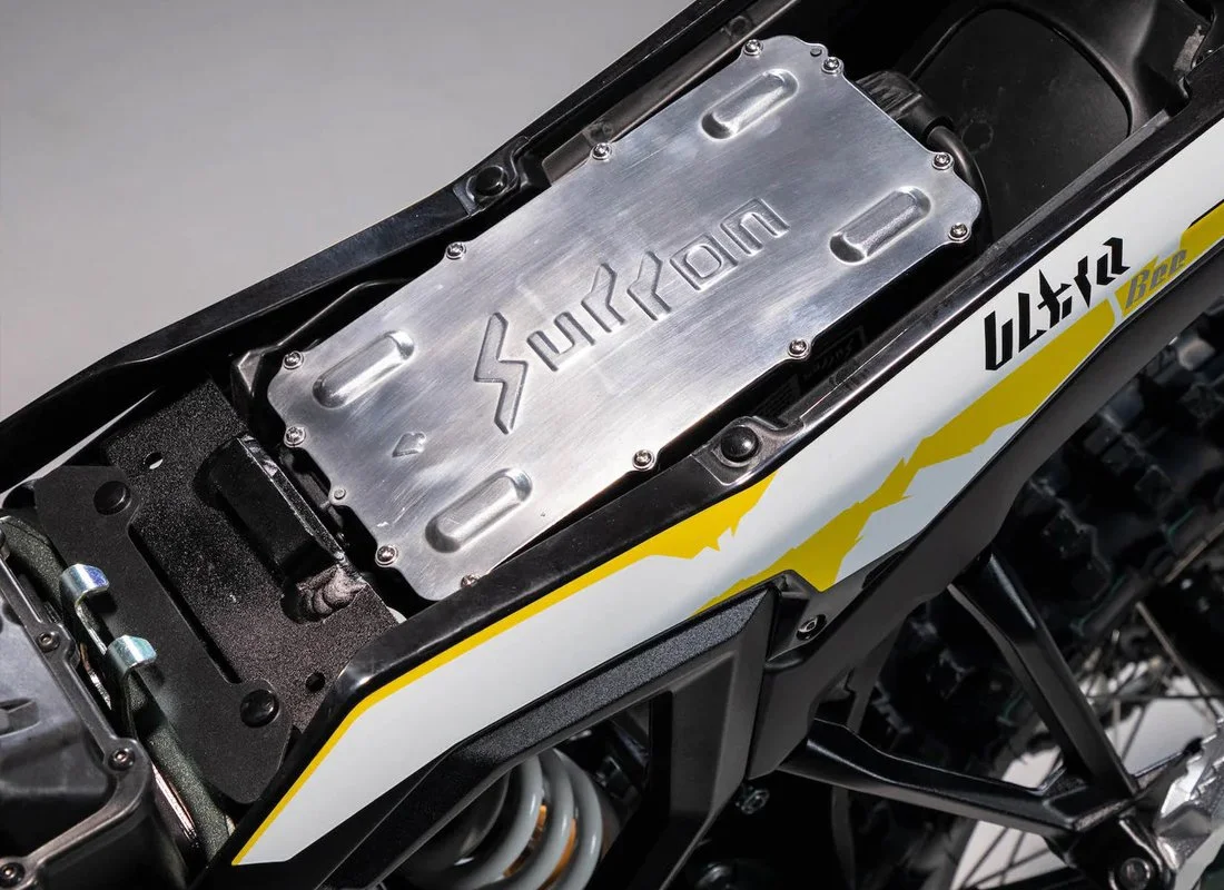 Close-up of a motorcycle engine with a metallic cover marked 'Sportron' in a partially exposed black frame and yellow and white bodywork.