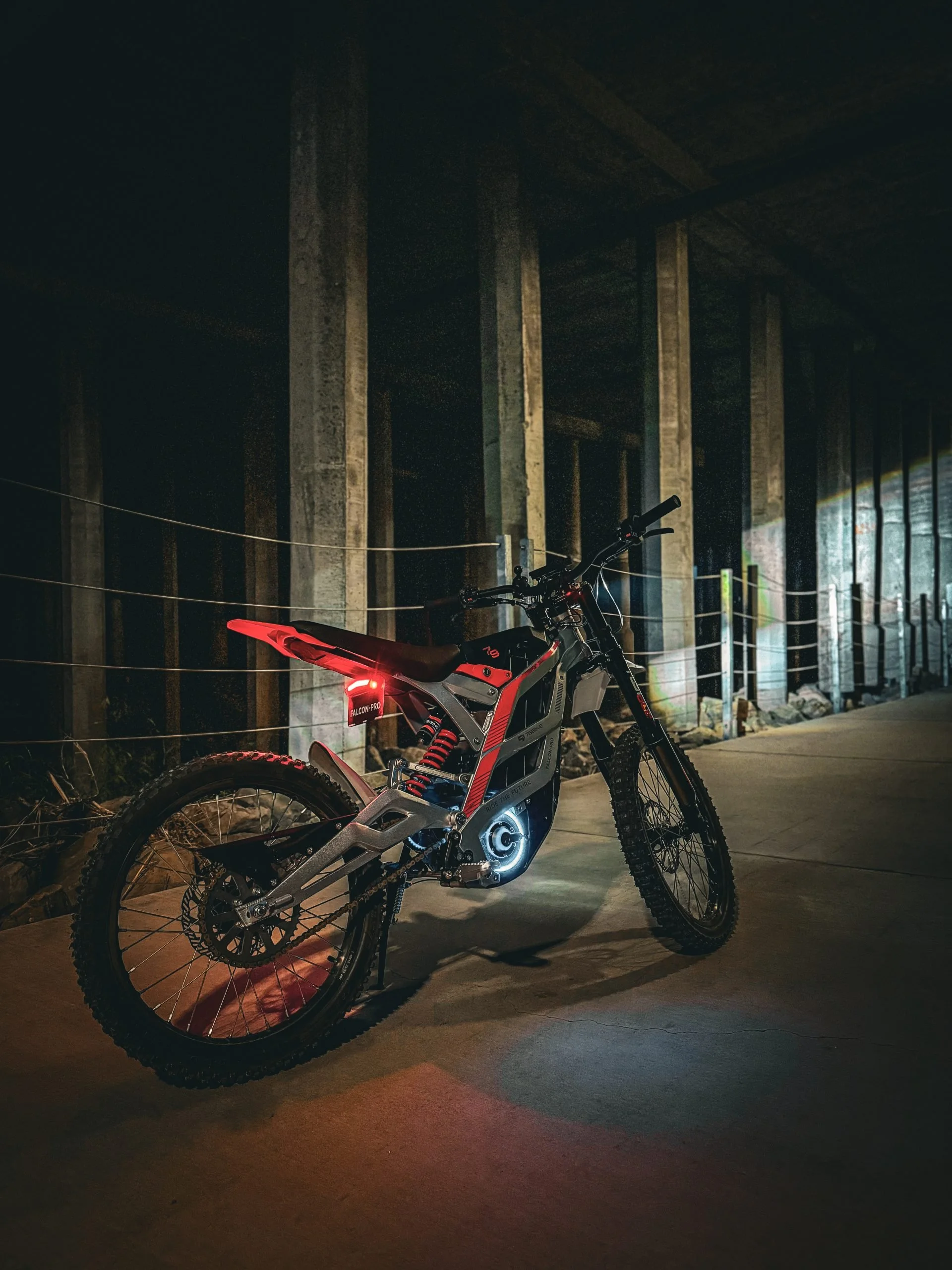 Electric mountain bike with illuminated lights parked under a concrete structure at night.