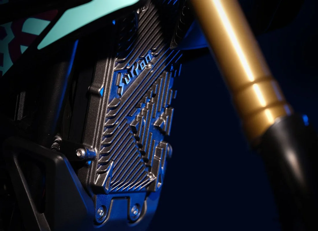 Close-up of a black electronic component with the word "Arduino" inscribed, mounted on a structure with a gold-colored fork and a colorful part in the upper left corner.