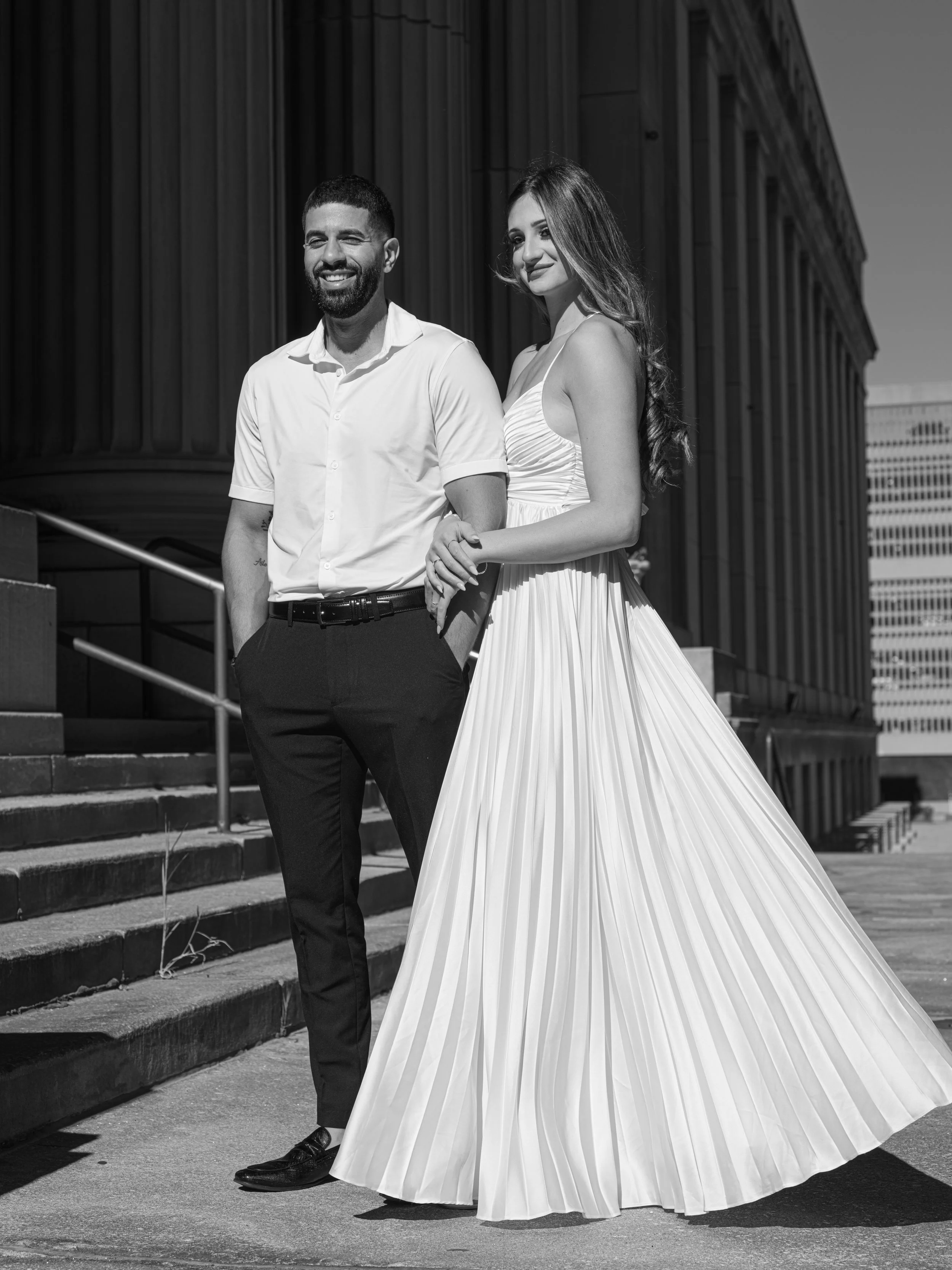 A smiling man and a woman in a flowing dress standing outside a large classical building