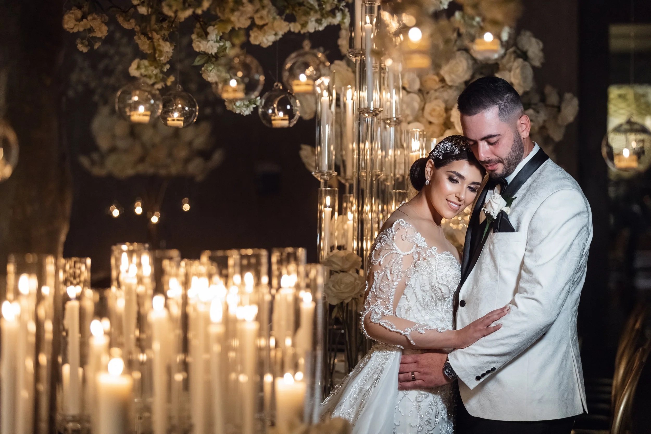 A bride and groom share an intimate moment at their wedding reception, surrounded by candles, flowers, and elegant decor.