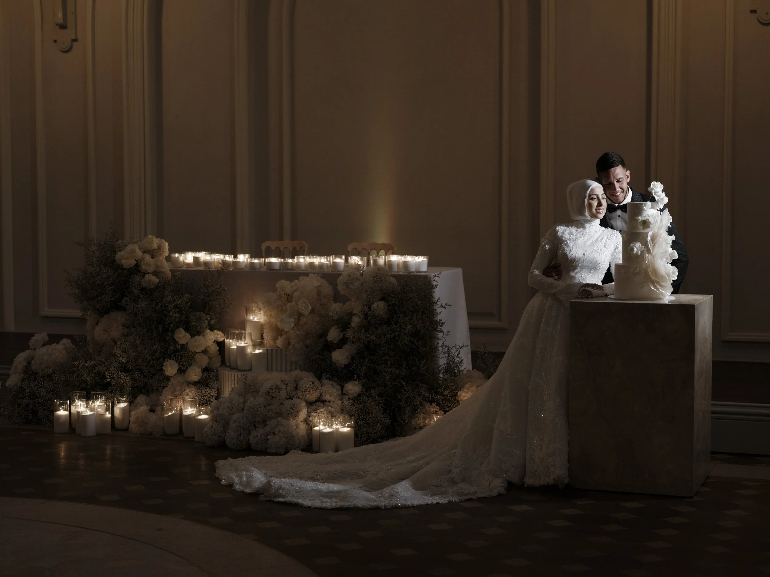 A bride and groom sharing a first dance at their wedding reception, surrounded by white floral arrangements and candles.