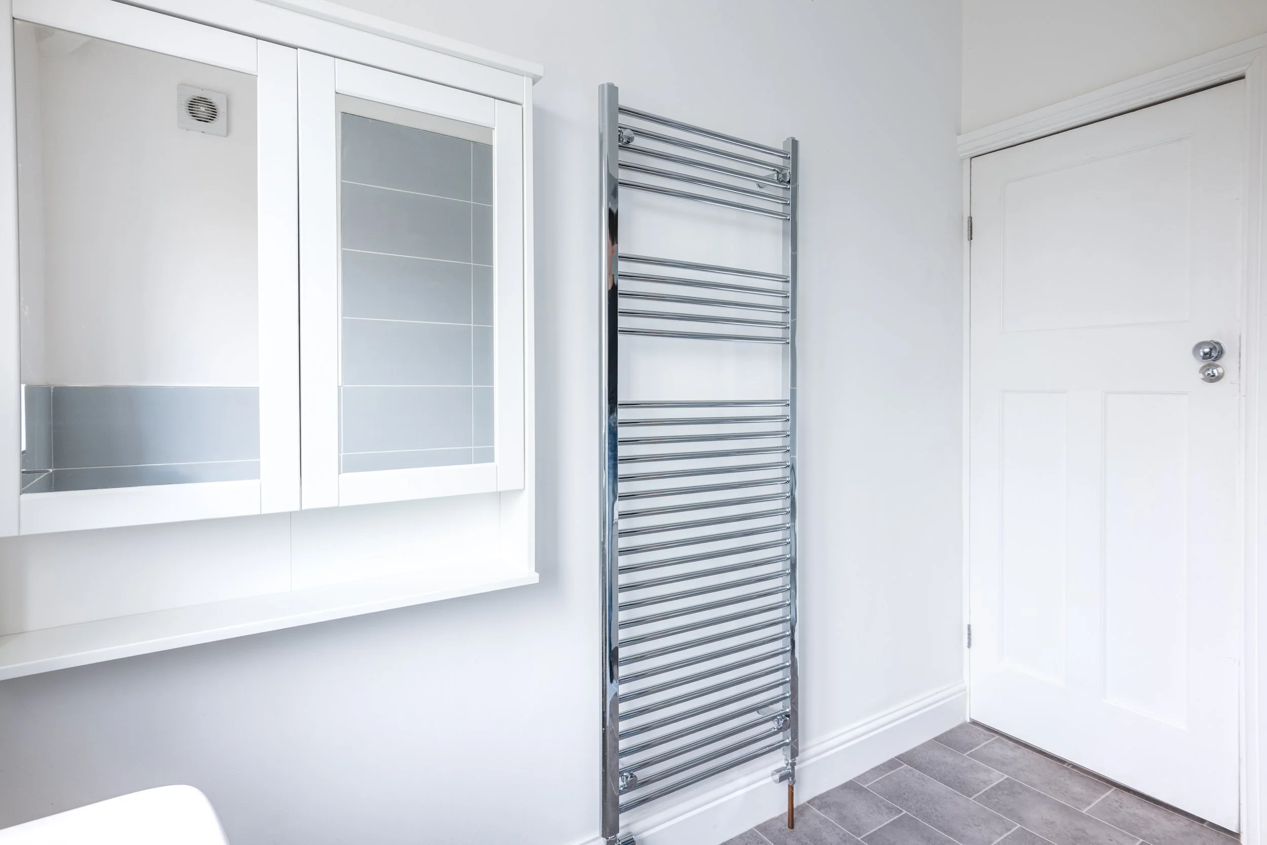 Bathroom with white cabinet, wall-mounted towel radiator, and closed white door.