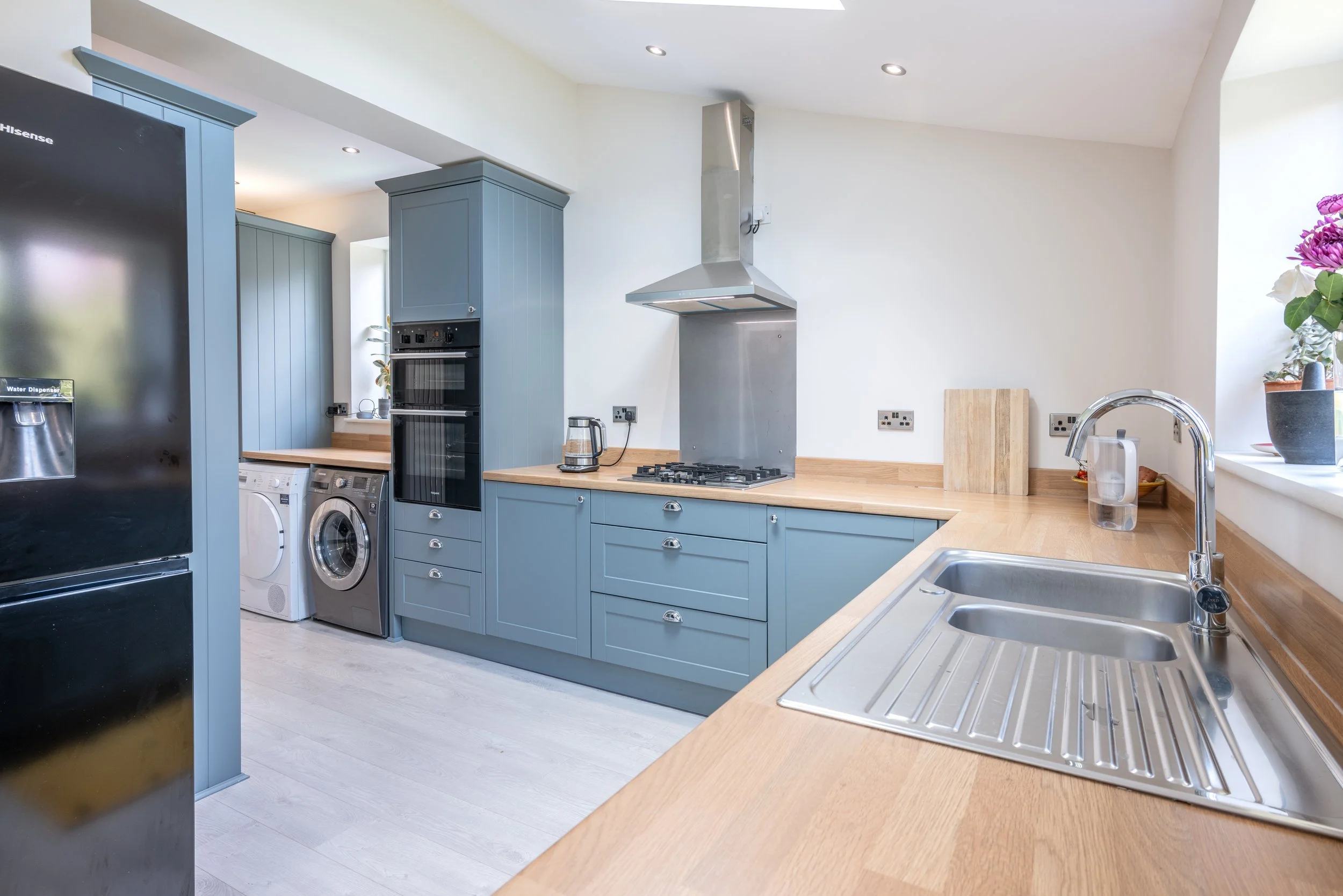 Modern kitchen with blue cabinets, a stainless steel stove, and a double sink near a window with flowers.
