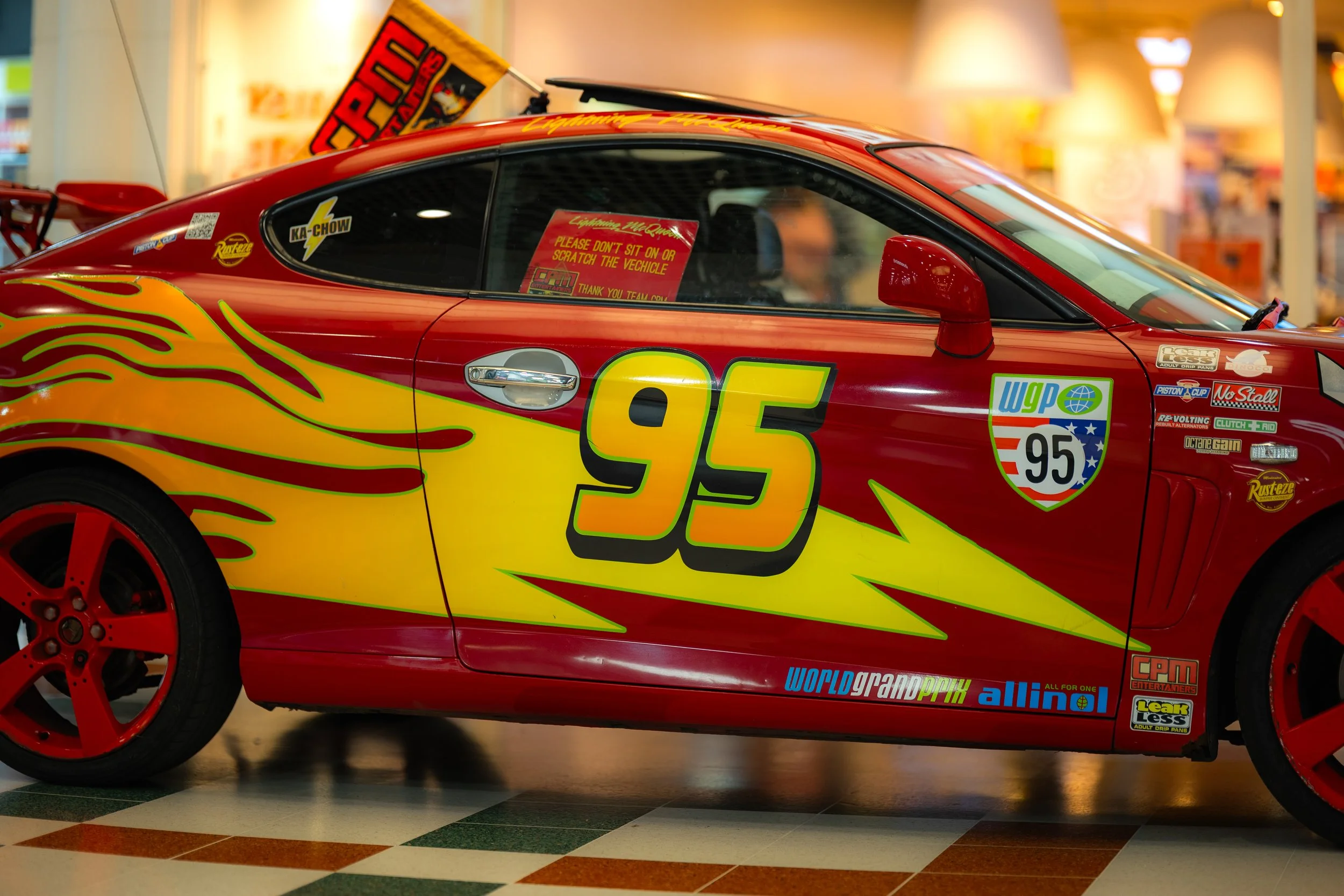 A red race car with yellow and orange flames and the number 95 on the side, displayed indoors on a tiled floor.