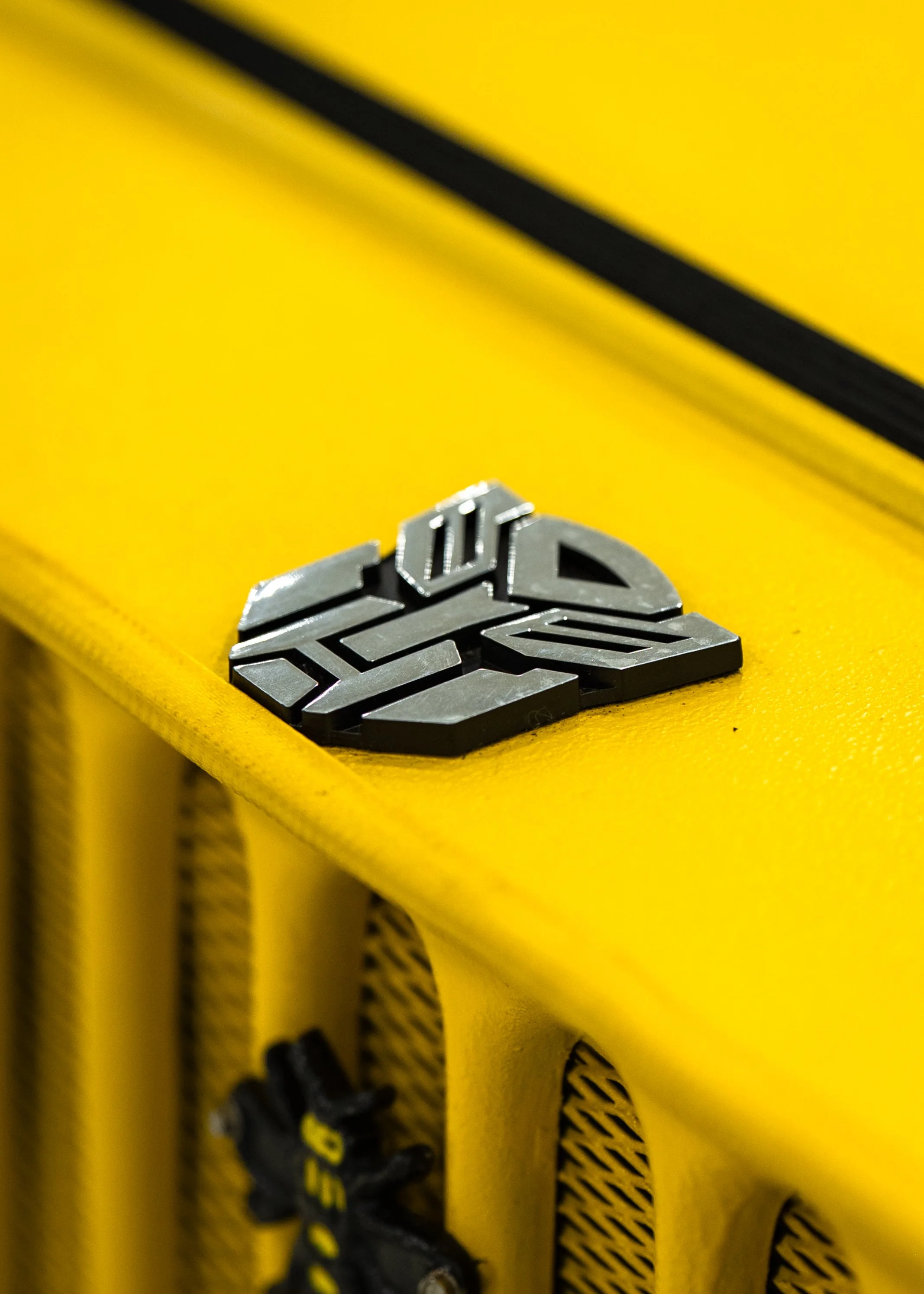 Close-up of a yellow industrial or construction piece of equipment with a metallic logo or emblem attached to the surface.