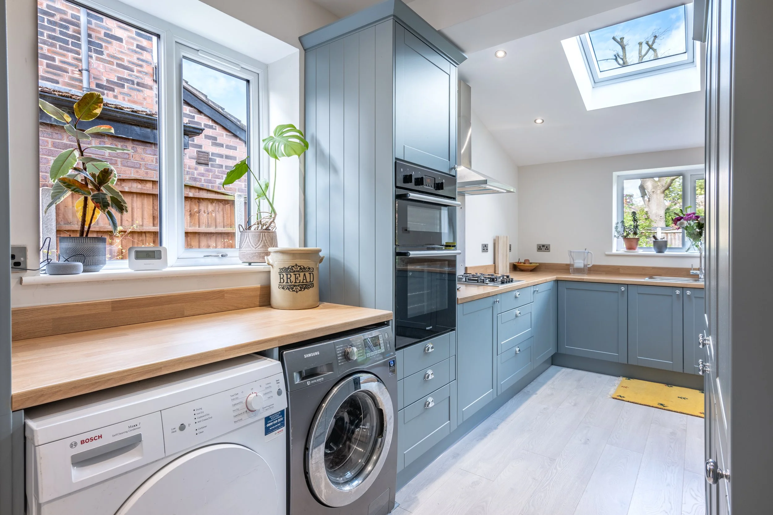 Modern kitchen with blue cabinets, wooden countertops, a washing machine, a dryer, and large windows and skylight letting in natural light.