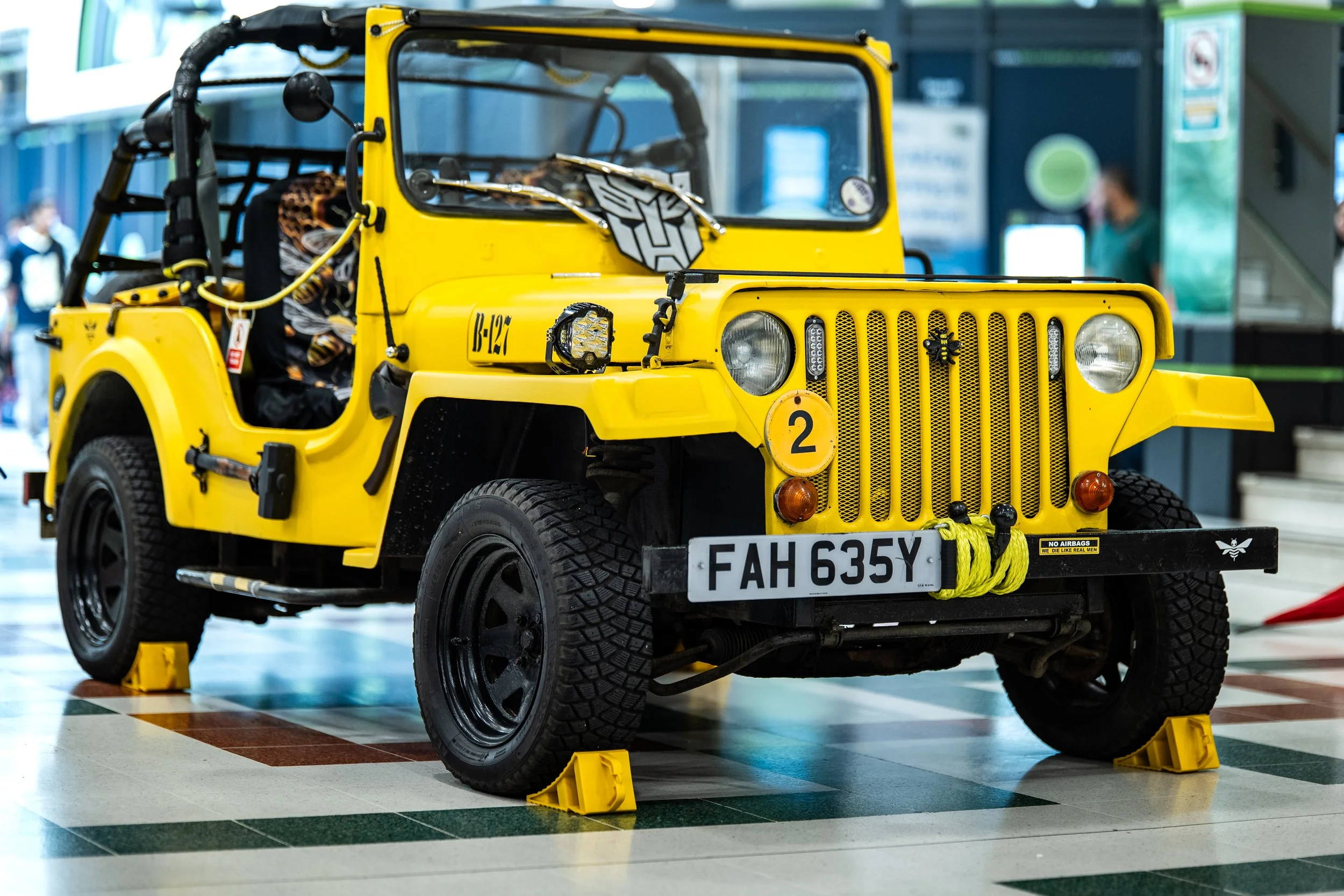 Yellow military-style jeep on display indoors with yellow wheel chocks and a license plate FAH 635Y.