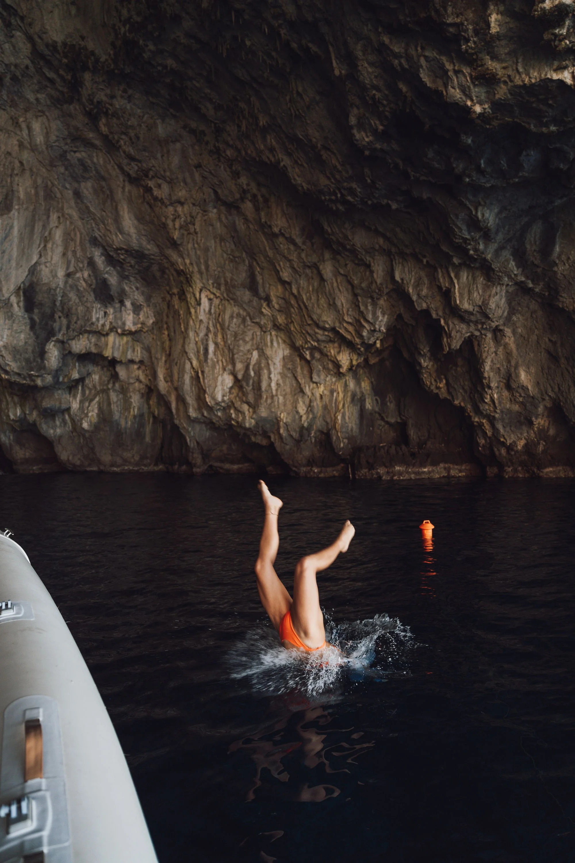 Person diving into water inside a large cave with rocky walls, wearing an orange swimsuit.