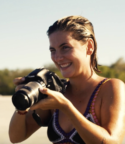 Woman smiling and holding a DSLR camera outdoors
