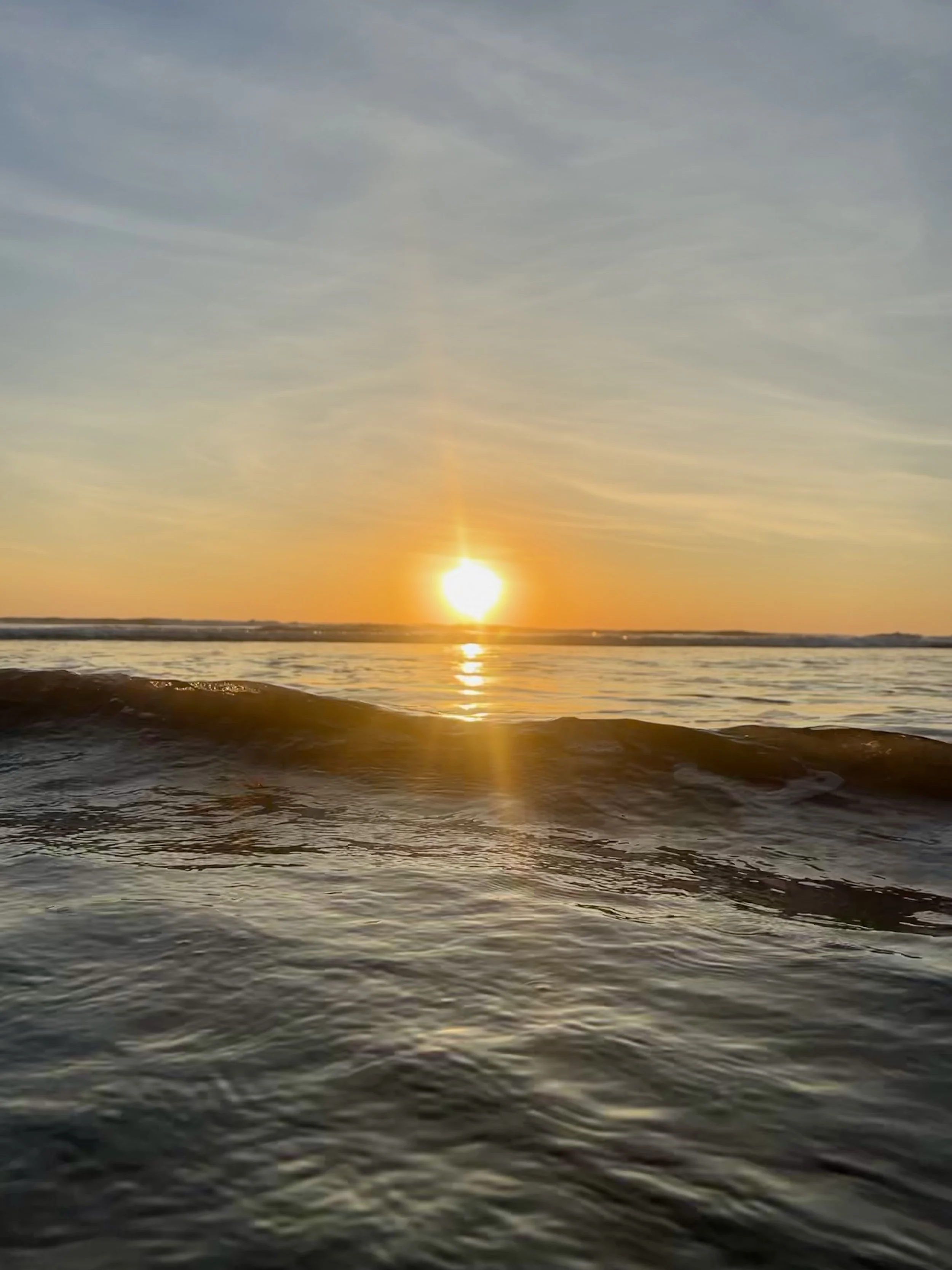 Sunset over ocean with waves in the foreground, sky with light clouds.