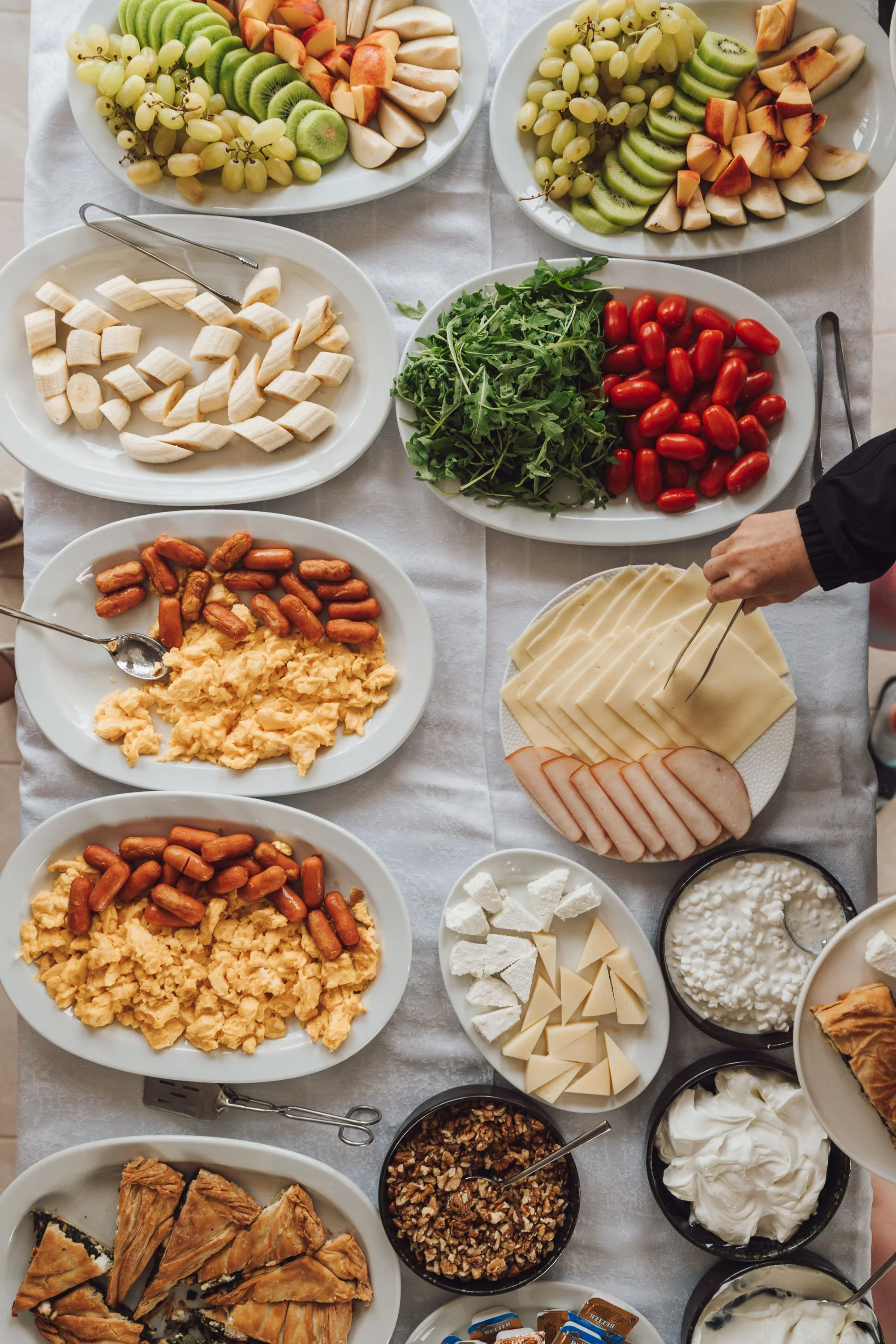 A table filled with various bowls of fruits, cheeses, vegetables, and other ingredients, possibly for a salad or a dish preparation.