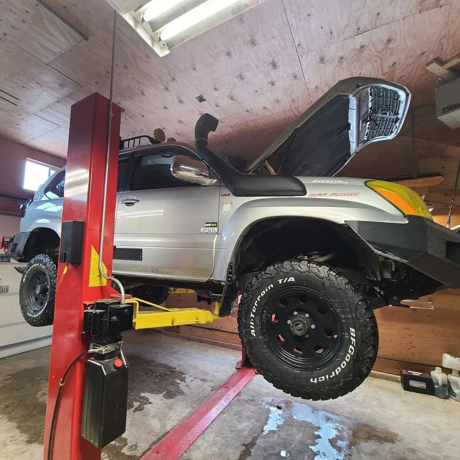 A silver off-road vehicle lifted on a hydraulic car lift