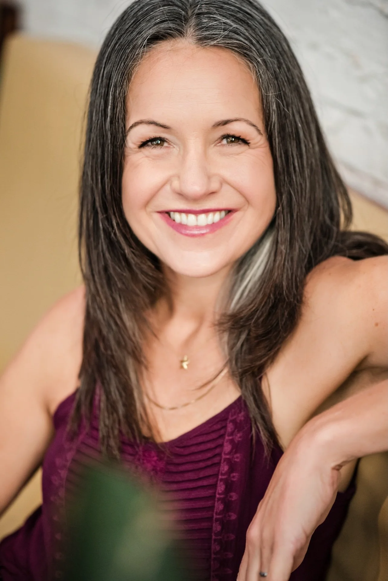 Relaxed and smiling author Anik St. Martin, D.C. indoor mid-shot portrait, woman with long dark hair wearing a purple dress and a gold necklace.