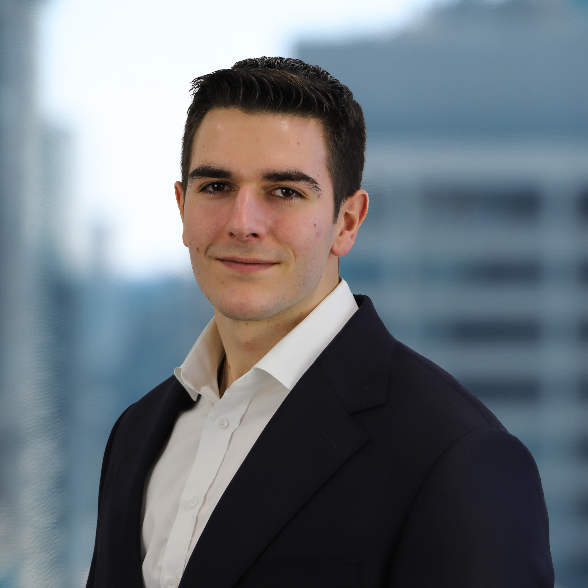 Professional young man in a suit standing in an office with a cityscape background.