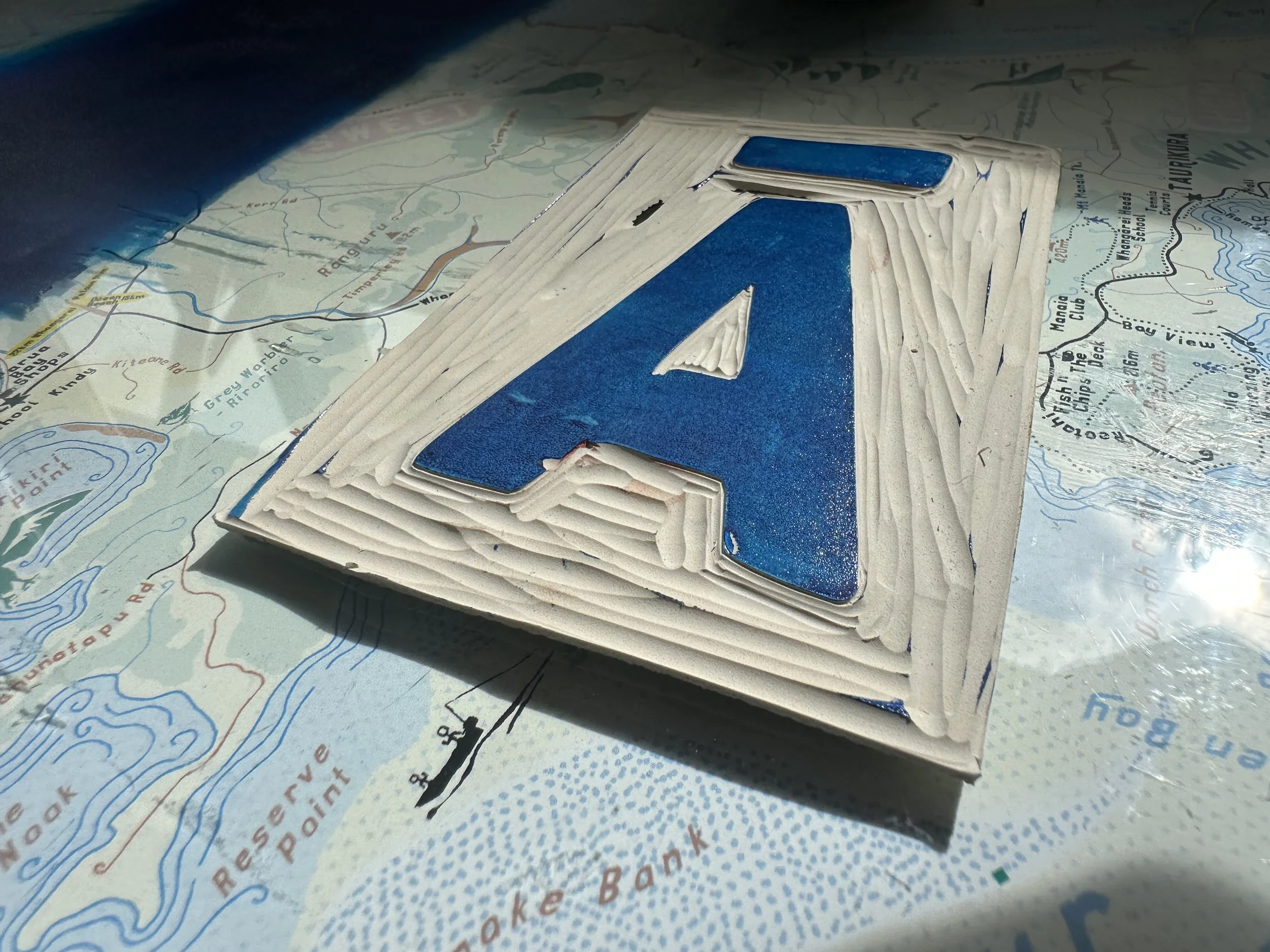 A large linocut blue letter 'A' with macron made of lino material, is placed on a colorful map.