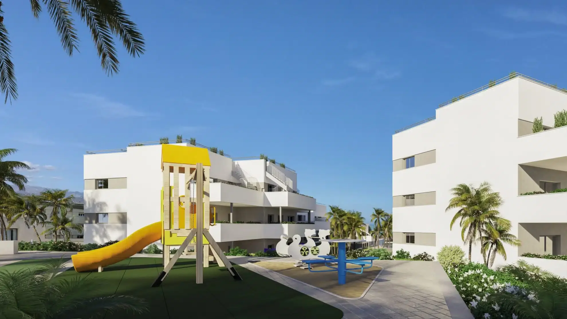 Modern white residential buildings with rooftop plants, a yellow slide in a landscaped courtyard, palm trees, and a playground with a blue roundabout at a sunny day.