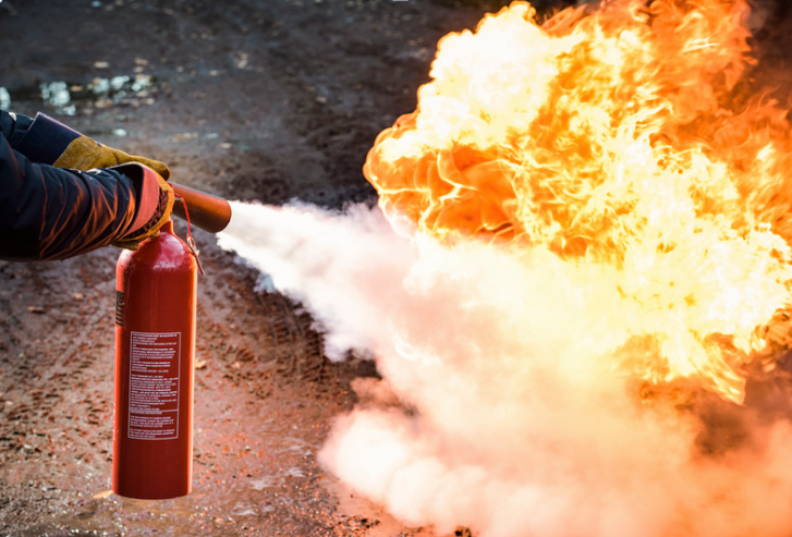 Person using a fire extinguisher to put out a fire on the ground.