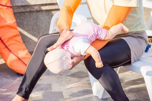 Person practicing infant CPR on a doll outdoors.
