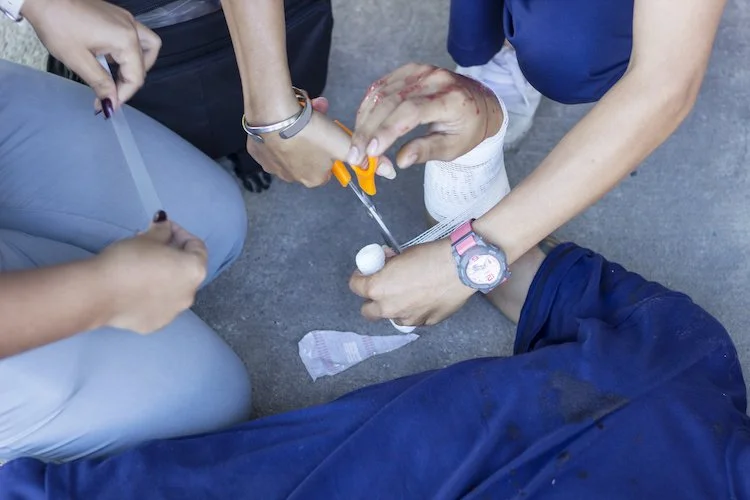 First responders provide medical aid to a person with an injured leg, including using scissors and bandages.