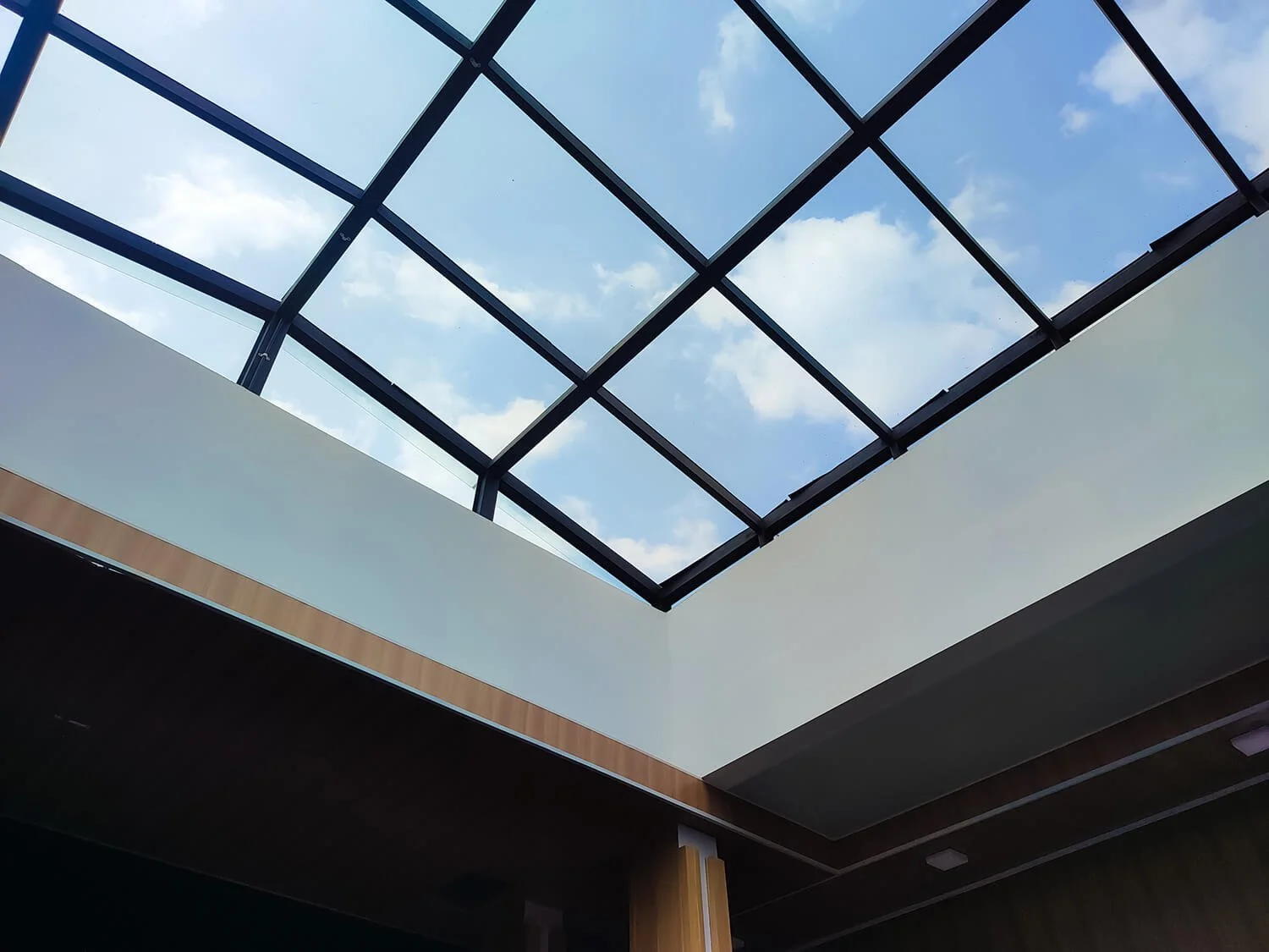 View of a glass ceiling with a blue sky and clouds seen through it.