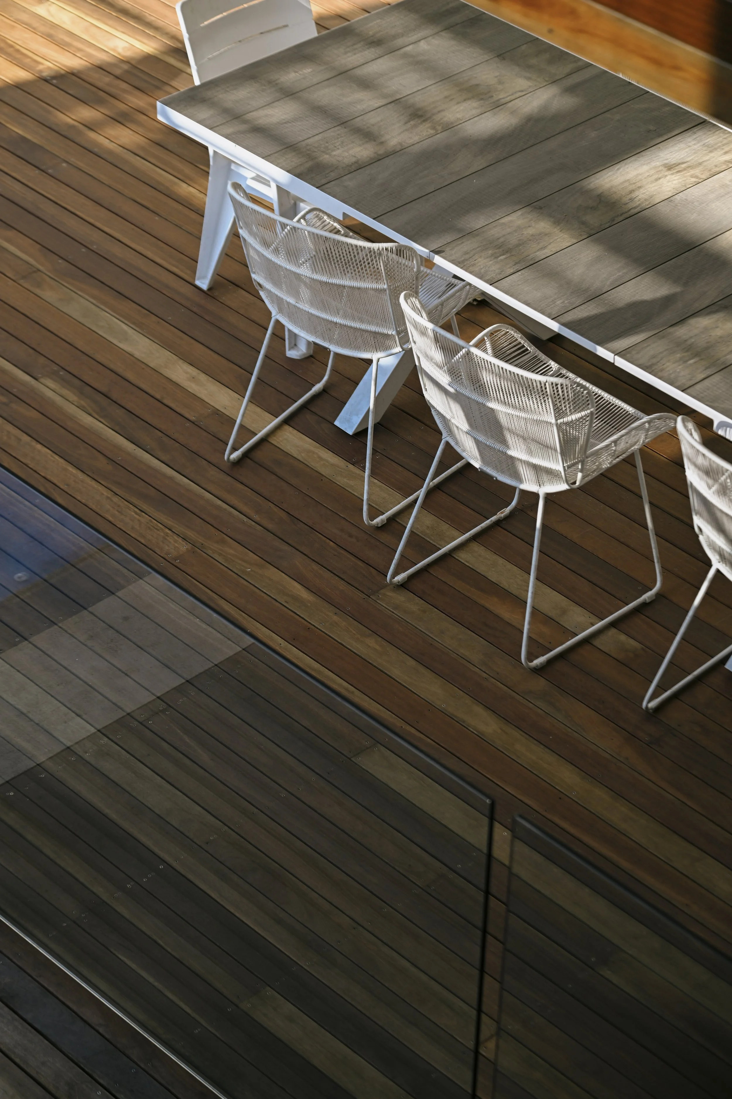 Wooden outdoor deck with a rectangular table and several white metal chairs