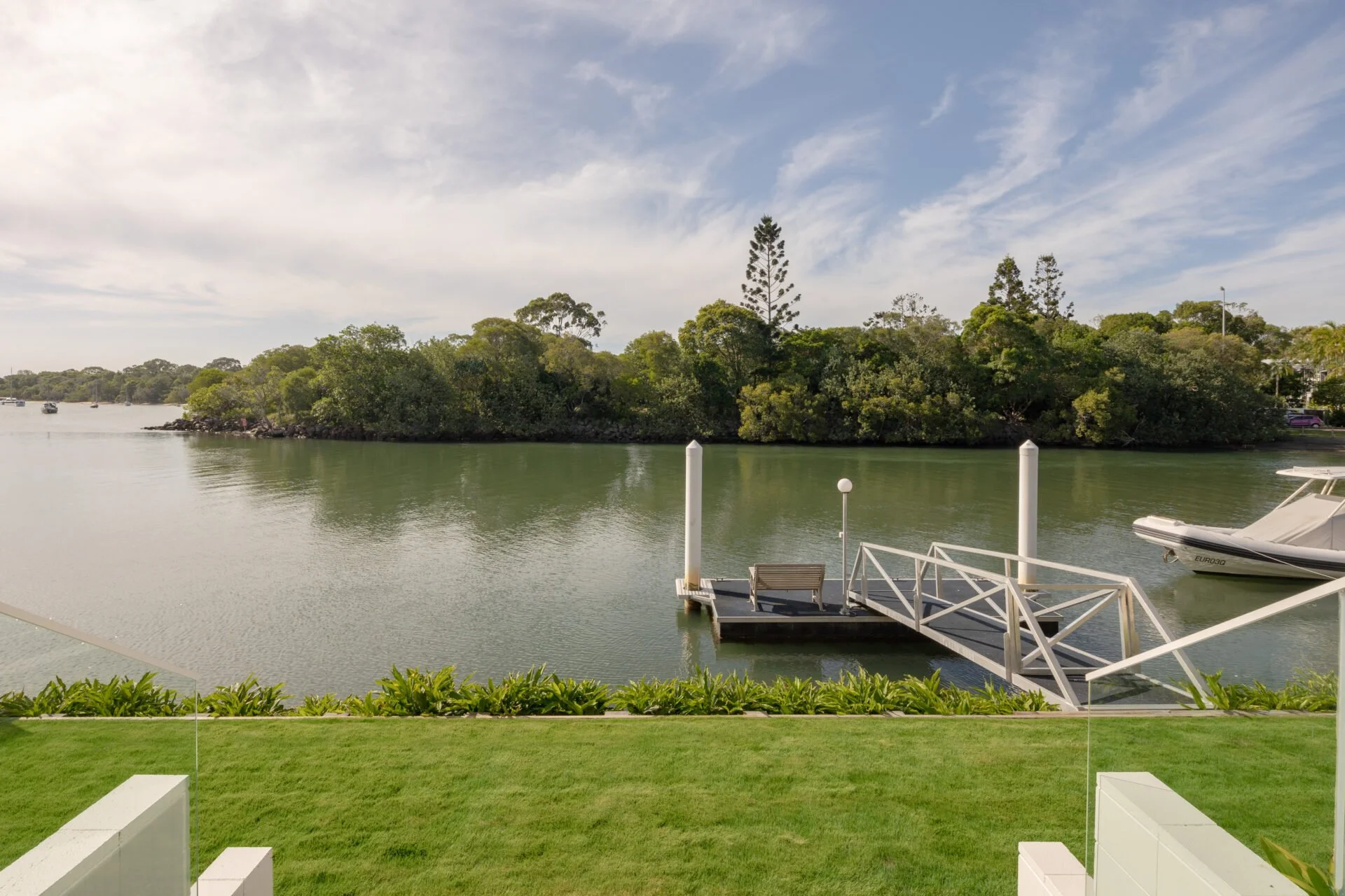 A lakeside scene with a boat dock, a small boat, and green trees across the water, under a partly cloudy sky.