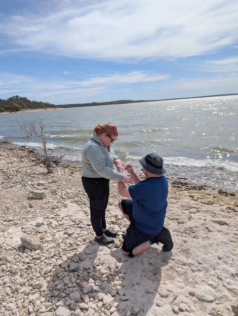 A man on one knee proposing to a woman on a rocky beach