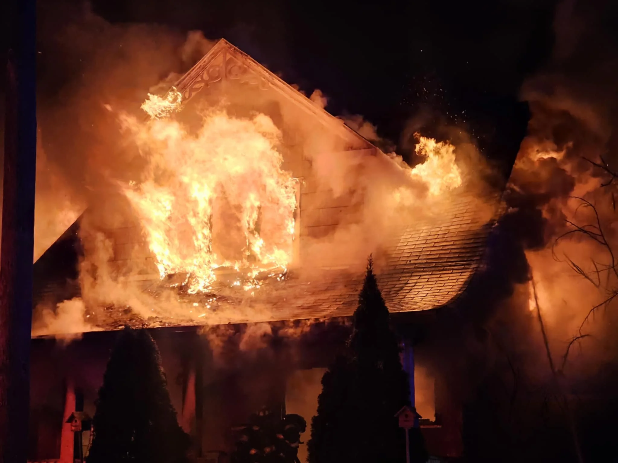 A house is on fire, with flames and smoke fully engulfing the building at night.