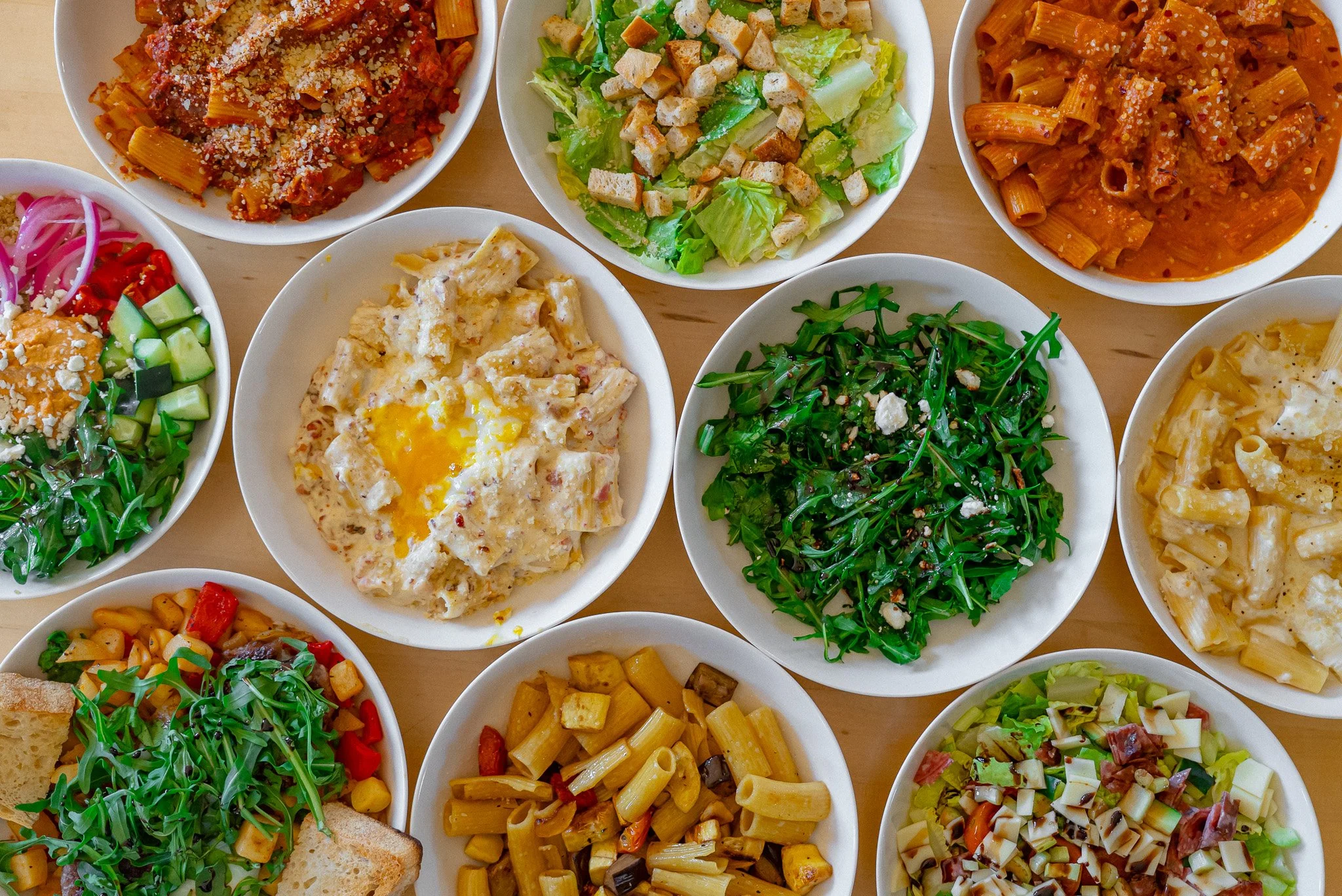 Assorted Italian pasta dishes with various salads and toppings on white plates.