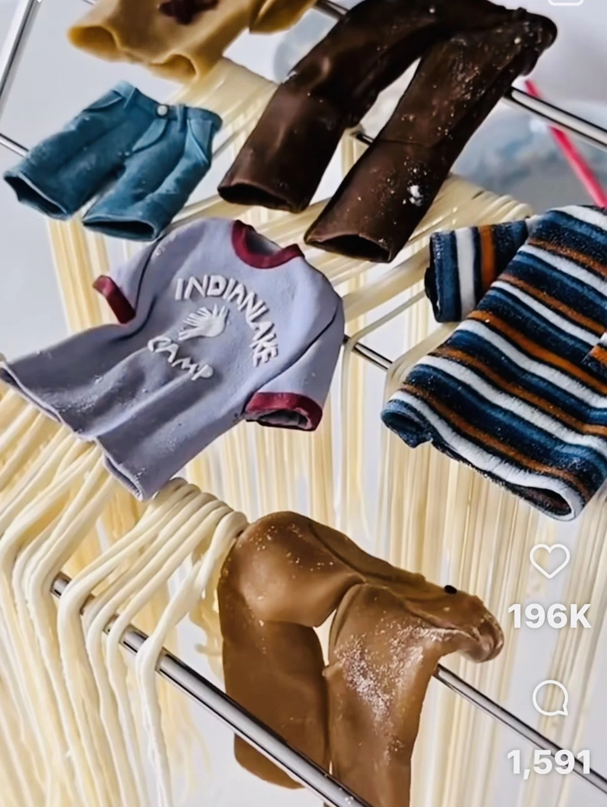 Clothes hang on a rack, including a striped shirt, a grey T-shirt with a handprint design, a pair of denim shorts, a yellow garment, and several large brown and black pieces of leather or fabric.