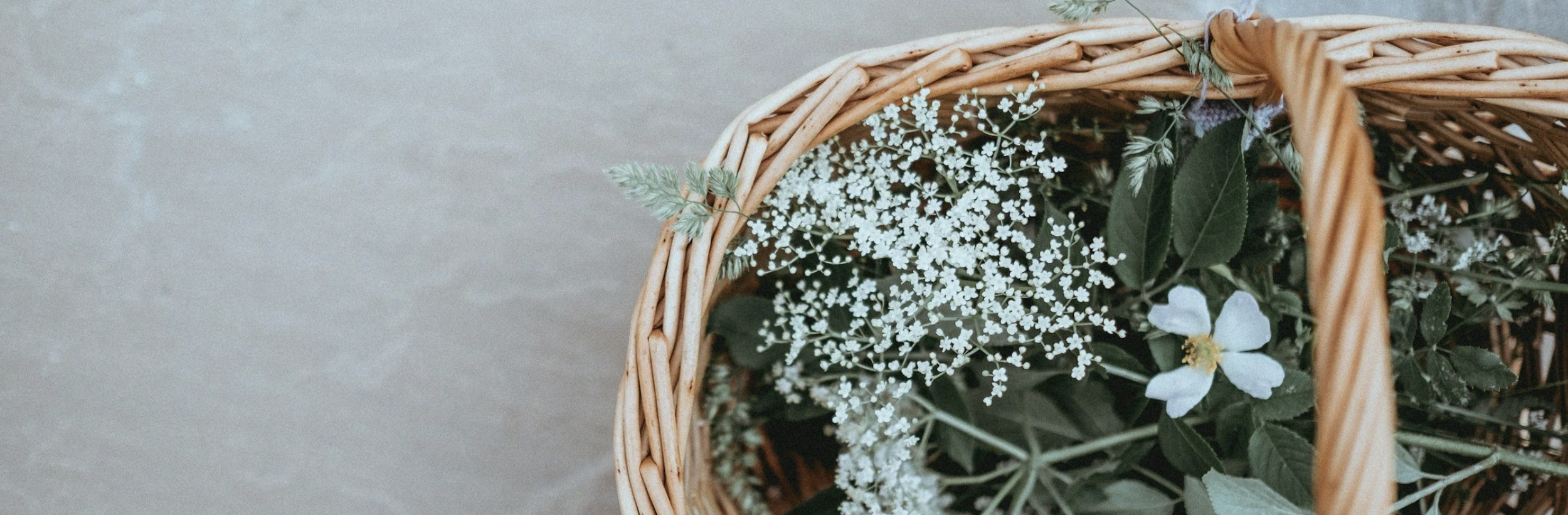 A wicker basket filled with white and green flowers and foliage, placed on a gray surface.