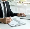 Businessperson in a suit working at a desk with a laptop and resume on a clipboard.