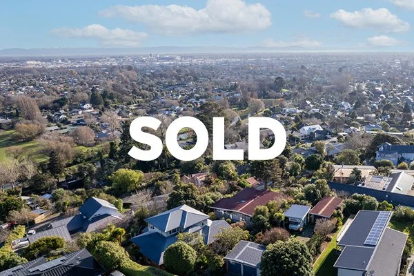 Aerial view of a suburban neighborhood with houses, trees, and green yards, under a partly cloudy sky, with 'SOLD' text overlay.