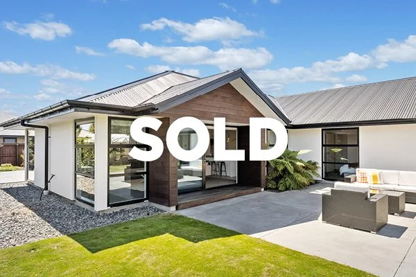 Modern house with a landscaped yard, outdoor seating area, and a large "SOLD" sign across the front.