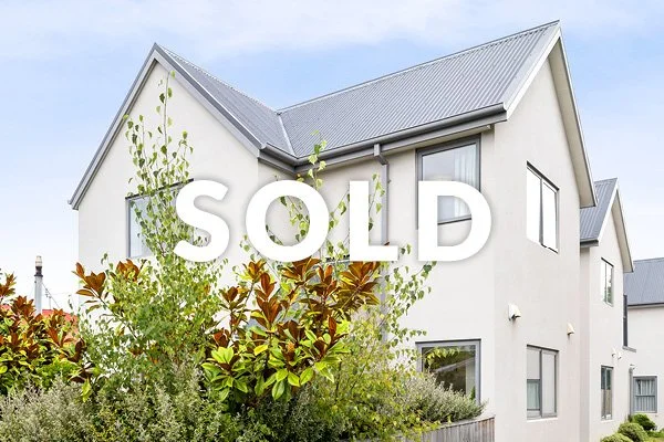 A white two-story house with a metallic roof, surrounded by greenery, with the word 'SOLD' overlaid.