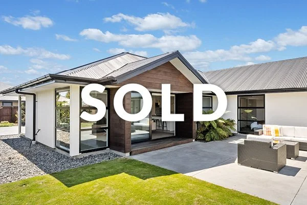 Modern house with a landscaped yard, outdoor seating area, and a large "SOLD" sign across the front.