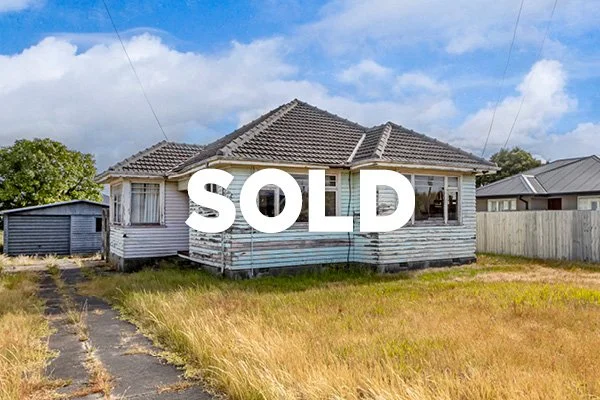 A weathered, abandoned house with a large 'SOLD' sign across it.