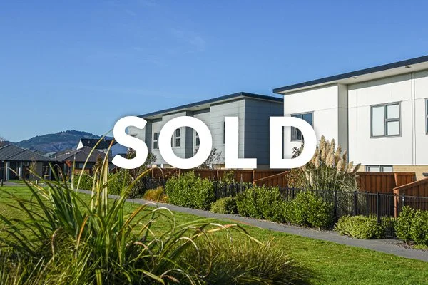 A new residential neighborhood with modern houses and landscaped gardens under a clear blue sky, with a large 'SOLD' sign across the image.