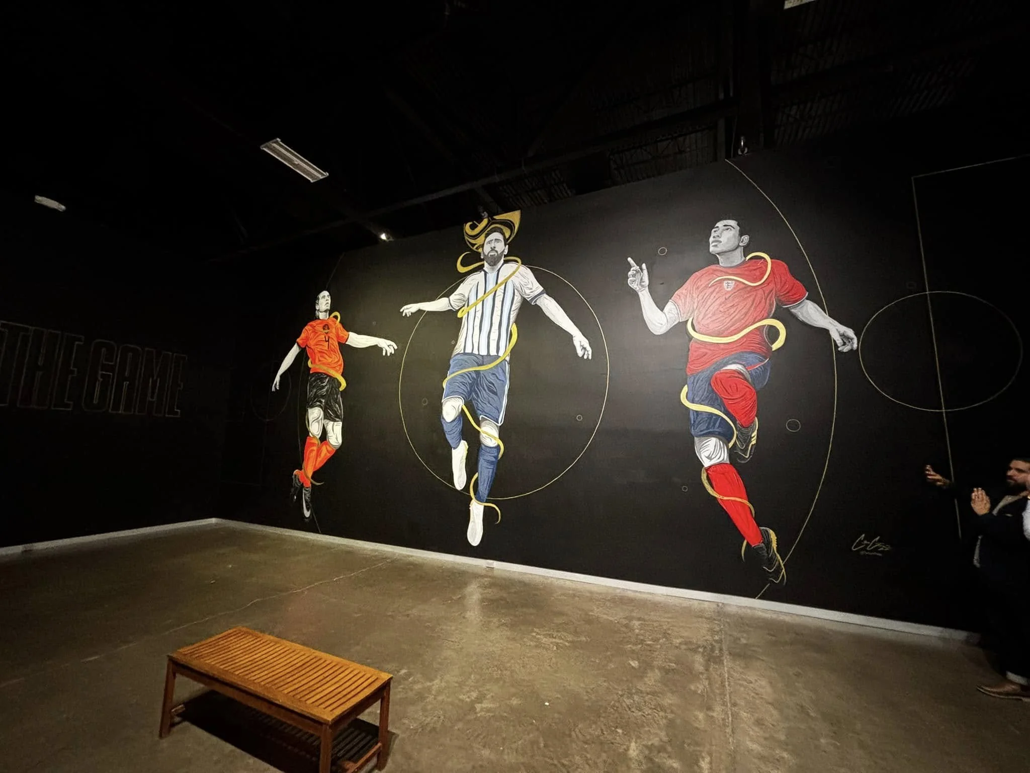 A mural depicting three soccer players in motion (Lionel Messi, Virgil Van Dyck, and Jude Bellingham) on a black background featured at the Arlington Museum of Art.